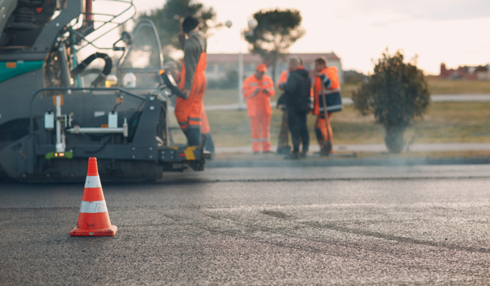 Asphalt paving. Paver machine and road cone and workers. New road construction.