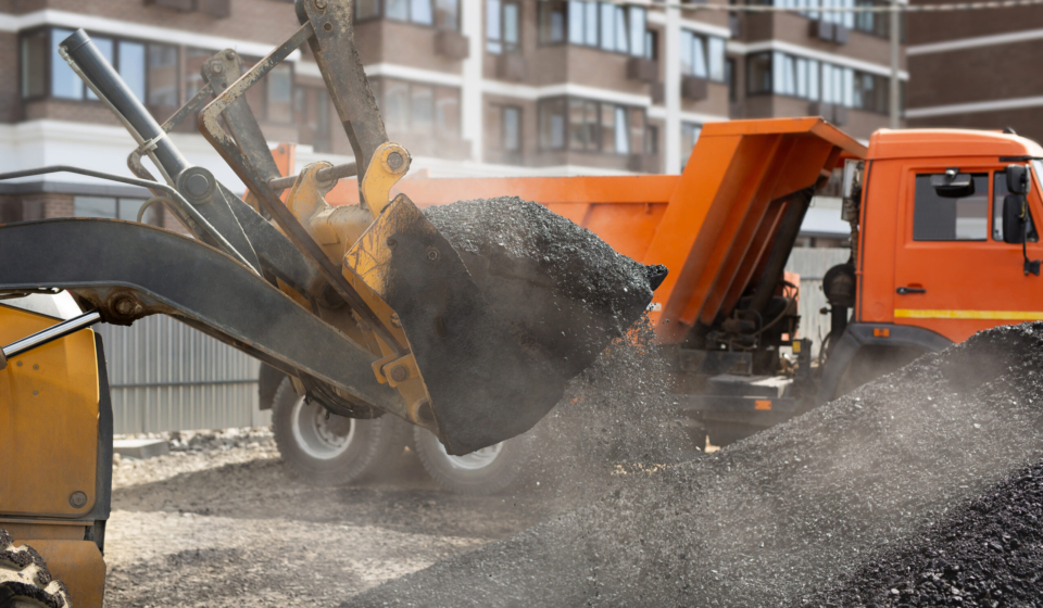 Construction of a new road, excavator bucket distributes hot asphalt on the road.