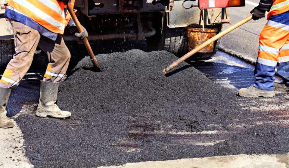 Road workers updating fresh hot asphalt with shovels and distribute it evenly over the surface